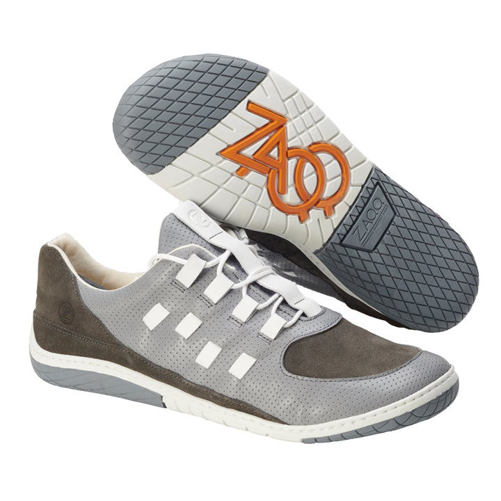 Wir präsentieren den BRISQ Grey von ZAQQ: Diese Sportschuhe kombinieren graues und braunes Nappaleder mit einer weißen Sohle. Die ZAQQ MINIMAL Sohle zeichnet sich durch ein markantes Profilmuster und ein orangefarbenes Logo aus, was ihnen noch mehr Attraktivität verleiht. Mit einem modernen Barfußschuh-Design zeigen diese Schuhe sowohl perforierte als auch glatte Texturen, die durch weiße Schnürsenkel elegant akzentuiert werden.