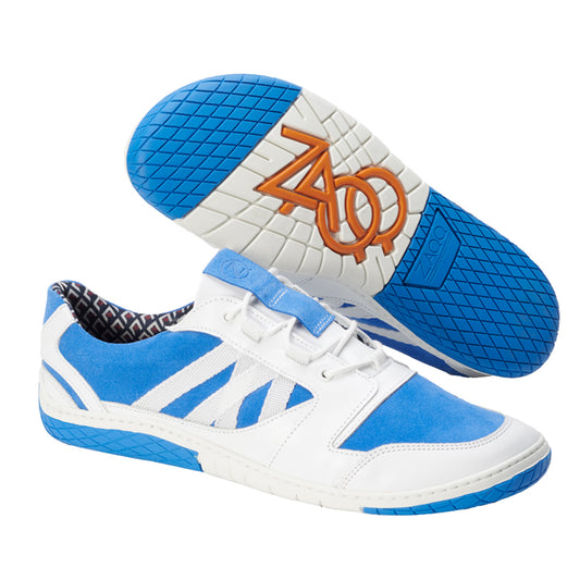 Wir präsentieren den QENDRIQ Blue von ZAQQ, ein Paar stylischer sommerlicher Sneaker. Diese Sneaker sind aus blauem Wildleder mit weißen Ledereinsätzen gefertigt und haben blaue Gummisohlen, die durch ein orangefarbenes Logo und ein gemustertes Innenfutter hervorgehoben werden. Das Design kombiniert gekonnt lässige und sportliche Elemente.