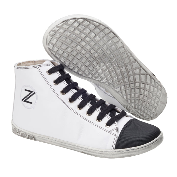 Wir präsentieren den CHUQQS White von ZAQQ, ein stilvolles Paar High-Top-Sneaker mit weißem Obermaterial, schwarzer Zehenkappe und schwarzen Schnürsenkeln. Diese Sneaker verfügen über eine strukturierte Sohle mit Gittermuster und zeigen das Z-Logo der Marke prominent an der Seite. Der weiße Sneaker verbindet nahtlos klassischen Stil mit modernem Komfort.