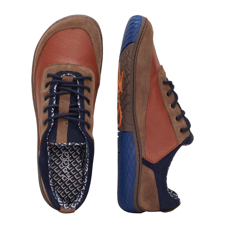 Der AQTIV Brown von ZAQQ ist ein Paar Freizeitschuhe, inspiriert vom Barfußschuh-Stil, mit einem strukturierten Obermaterial aus braunem Leder mit Akzenten aus marineblauem Wildleder und passenden marineblauen Schnürsenkeln. Die blauen Sohlen sind seitlich mit einem orangefarbenen Muster hervorgehoben, während das Innere ein geometrisches Design für verbesserte Atmungsaktivität aufweist.