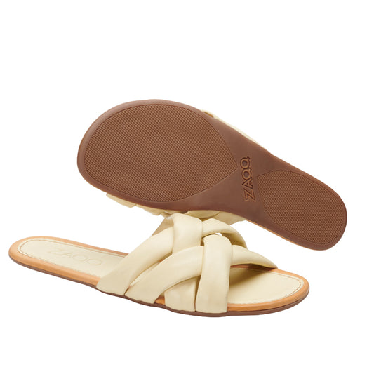 Ein Paar ZAQQ ALAQ Beige Slipper-Sandalen mit geflochtenen Riemen und braunen Kautschuk-Sohlen. Eine Sandale ist so positioniert, dass die strukturierte Sohle zur Geltung kommt, während die andere die Draufsicht bietet. Der Markenname ist sowohl auf der Innensohle als auch auf der Sohle deutlich zu sehen und betont das Barfußsandale-Design.