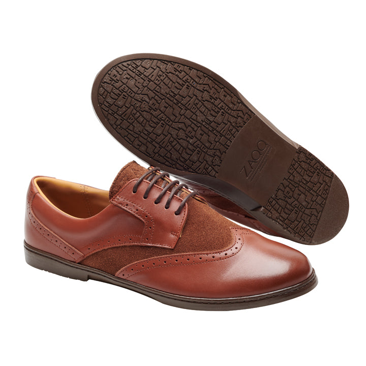 Der „BRIQ Brogue Antique Cognac“ von ZAQQ ist ein Paar braune Business-Oxford-Schuhe aus hochwertigem Kalbsleder. Ein Schuh steht aufrecht und zeigt die exquisite Brogue-Verzierung, während der andere schräg steht, um die aufwendig strukturierte Sohle hervorzuheben.