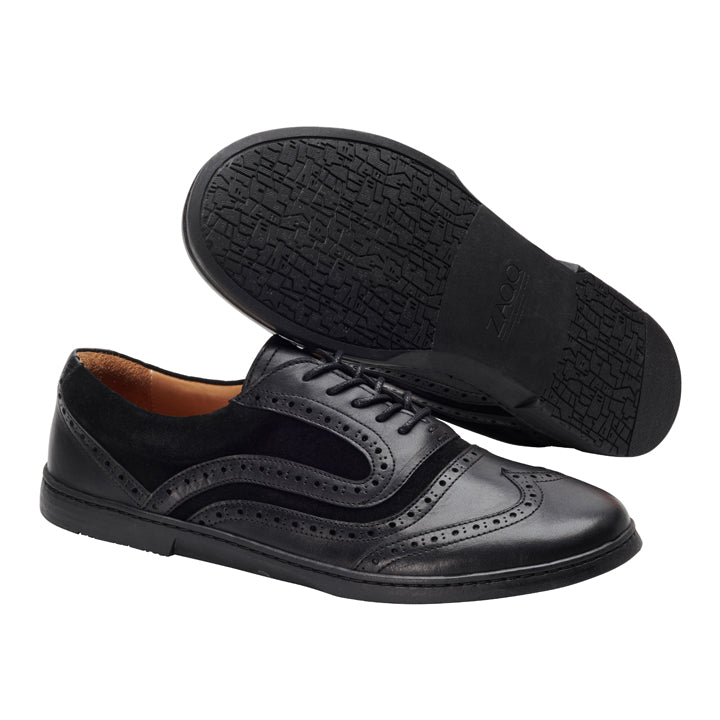 Die BRIQ Brogue Deep Black von ZAQQ sind schwarze Businessschuhe aus Leder mit dekorativen Perforationen und einem Schnürdesign. Aus hochwertigem Kalbsleder gefertigt, wird ein Schuh aufrecht präsentiert, während der andere die strukturierte Sohle zur Schau stellt, was ihren formellen und stilvollen Reiz unterstreicht.