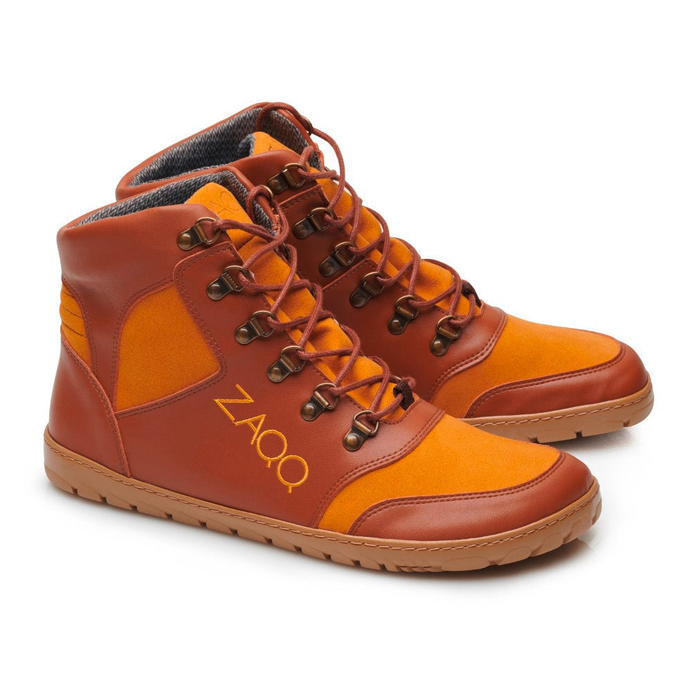 Die HIQE Vegan Sierra Waterproof Sneaker haben ein High-Top-Design in Orange- und Brauntönen, ergänzt durch orangefarbene Schnürsenkel. Inspiriert von Barfußschuhen weisen sie eine strukturierte Sohle und Metallösen auf. Der Markenname ZAQQ ist elegant in Gold auf der Seite aufgedruckt und bietet Stil und Komfort für Personen, die ein natürliches Gehgefühl schätzen.