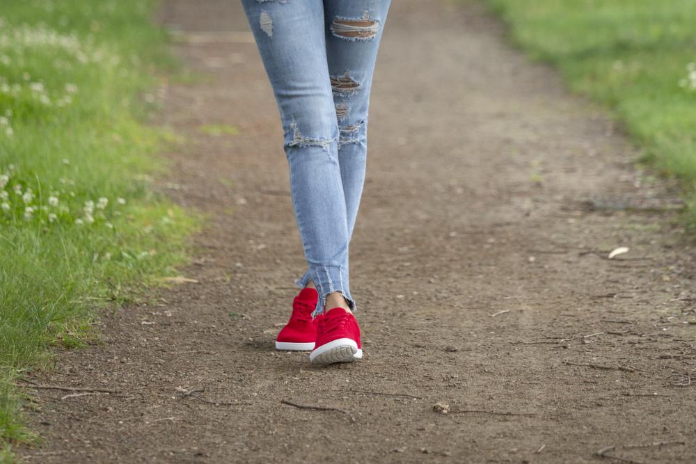 Eine Person in zerschlissenen Bluejeans und einem Paar roter LIQE Race-Sneaker von ZAQQ läuft einen Feldweg entlang, der von Gras umgeben ist. Das Bild betont ihre Beine und Füße, fängt die Bewegung ein und hebt eine lässige Umgebung im Freien hervor, die ideal ist, um die neuen LIQE Race-Sneaker einzulaufen.