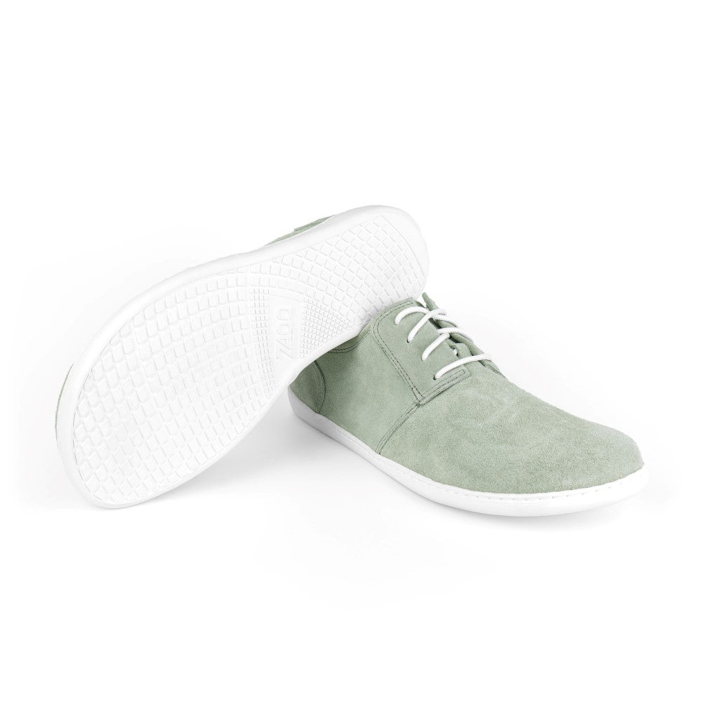 Ein Paar PIQUANT Velours LichtGrey-Sneaker von ZAQQ verfügt über ein elegantes Veloursleder-Finish mit weißen Sohlen und Schnürsenkeln. Ein Schuh steht aufrecht, während der andere auf die Seite geneigt ist, wodurch die strukturierte Sohle vor einem schlichten weißen Hintergrund hervorgehoben wird.