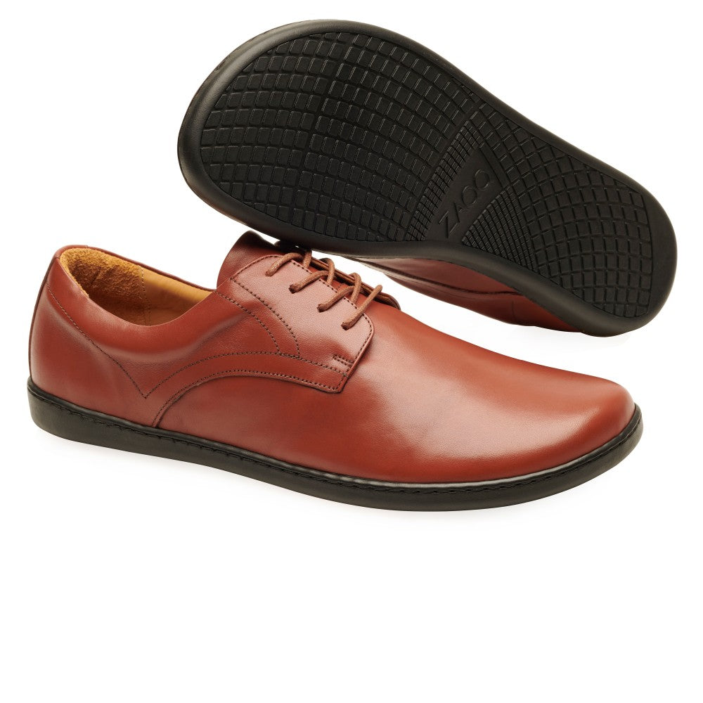 Ein Paar stilvolle ZAQQ PEAQ Cognac Lederschuhe mit schwarzer Gummisohle. Ein Schuh steht aufrecht, während der andere sein strukturiertes Barfußsohle-Muster hervorhebt. Das polierte Glattleder-Finish und das Schnürdesign unterstreichen ihr anspruchsvolles Erscheinungsbild.