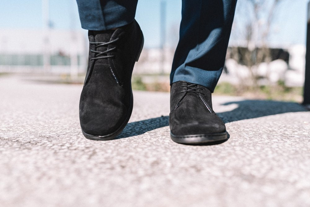 Nahaufnahme einer Person, die auf einem strukturierten Bürgersteig läuft und die stilvollen schwarzen Business-Schuhe QLASSY von ZAQQ und eine blaue Hose trägt. Der Hintergrund ist unscharf, sodass die Bewegung und der Schuhstil im Vordergrund stehen.