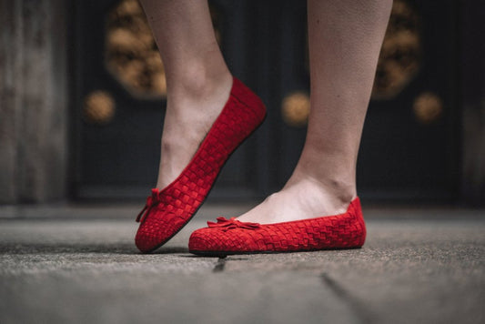 Ein Paar flache Schuhe ZAQQ TWIST Red mit gewebter Textur und einer kleinen Schleife auf der Vorderseite. Der Barfuß-Ballerina-Stil bietet Komfort, wobei ein Schuh die Seitenansicht zeigt und der andere die schwarze Sohle freigibt.