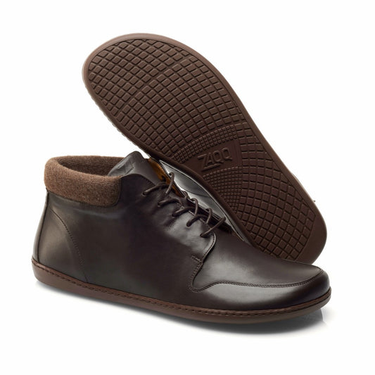 Ein Paar NEWQUAY Brown High-Top-Schuhe von ZAQQ mit dunkelbraunem Nappaleder-Finish, braunen Schnürsenkeln und einem weich gepolsterten Knöchelkragen. Ein Schuh steht aufrecht, während der andere geneigt ist, um die Waffelsohle mit dem ZAQQ-Logo zu zeigen. Diese Barfußschuhe bieten außergewöhnlichen Komfort für den täglichen Gebrauch.