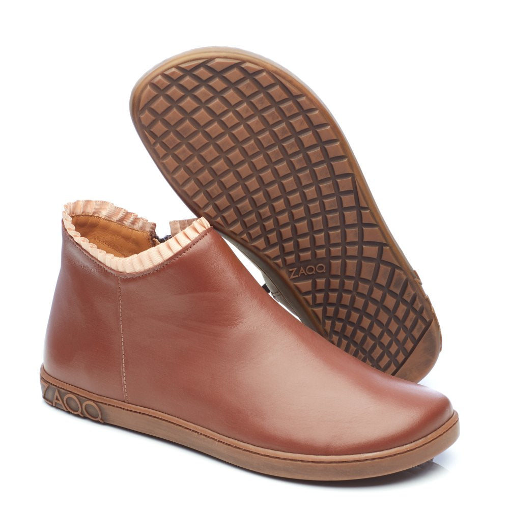 Die CHOQQO Brown Stiefeletten von ZAQQ haben eine flexible Barfußsohle und sind aus braunem Leder gefertigt. Die Abbildung zeigt einen Stiefel aufrecht und den anderen mit der kreuzgemusterten Sohle. Die Marke ZAQQ ist sowohl auf der Rückseite als auch auf der Sohle deutlich sichtbar und sorgt für Komfort bei jedem Schritt.