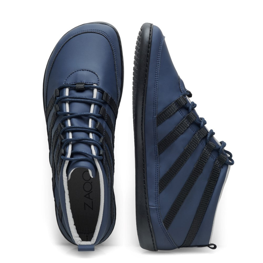 Abgebildet ist ein Paar SPARQ Mid Dark Blue High-Top-Sneaker in sportlichem Design. Ein Schuh steht vertikal und zeigt seine Seite mit schwarzen Schnürsenkeldetails und einer flexiblen Gummisohle, während der andere flach liegt und die Draufsicht zeigt. Der Markenname ZAQQ ist im Inneren des veganen Barfuß-Sneakers sichtbar.