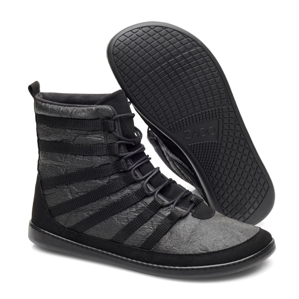 Die SPARQ High Pinatex Sneaker von ZAQQ bestechen durch ihr dynamisches Design in Schwarz und Grau. Diese modischen High-Tops sind mit dunklen Schnürsenkeln und einer Gummisohle mit aufwendigem Muster ausgestattet. Ein Sneaker steht aufrecht und betont sein Seitenprofil, während der andere flach liegt und das detaillierte Profil der Sohle zur Schau stellt.