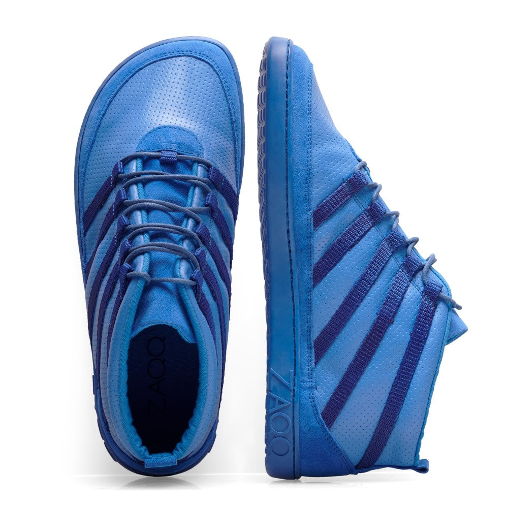 Präsentiert werden die SPARQ Mid Azure Sneaker von ZAQQ, gefertigt aus blauem Nappaleder mit perforierter Textur und dunkelblauen Kontraststreifen. Sie zeichnen sich durch ein sichtbares Kautschuk-Sohle-Design aus. Ein Schuh steht aufrecht, während der andere auf der Seite liegt und so die Marke ZAQQ hervorhebt.